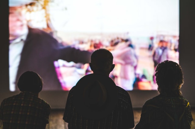 Silhouette of 3 people watching show on TV