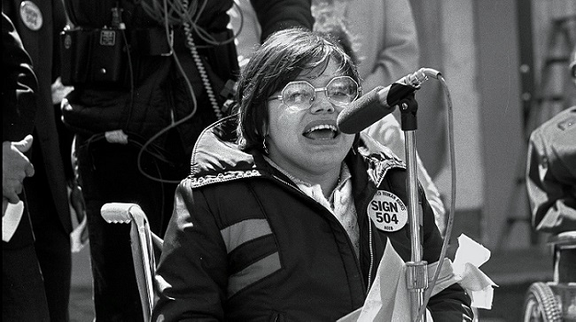 Black and white photo of activist Judy Heumann delivering a speech