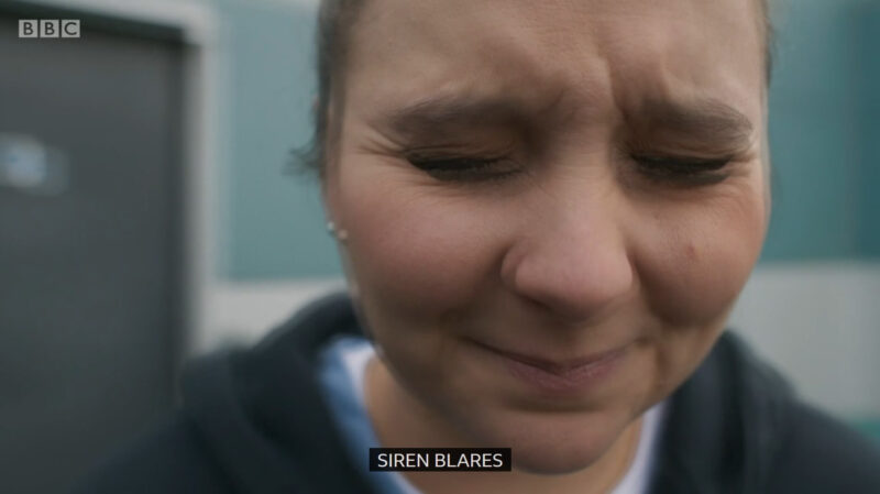 Clip of a Casualty episode where Jade has her eyes closed, the screen is fuzzy and blurred plus the caption at the bottom is "Siren blares"