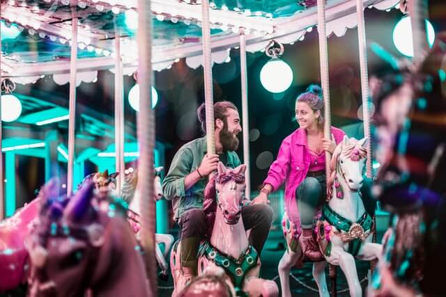 A man and woman holding hands on carousel riding on their own horses