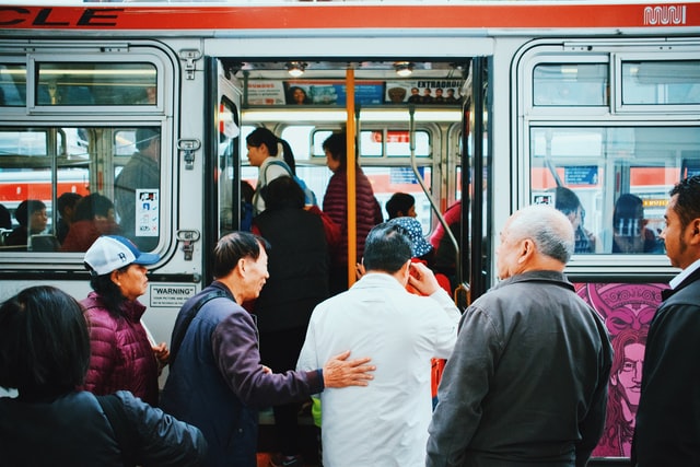 Photo of bus passengers getting on the bus, with one particular passenger placing his hand on another man's back